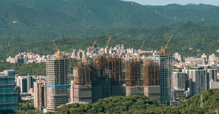 Aerial view of urban construction with cranes set against a mountain backdrop.